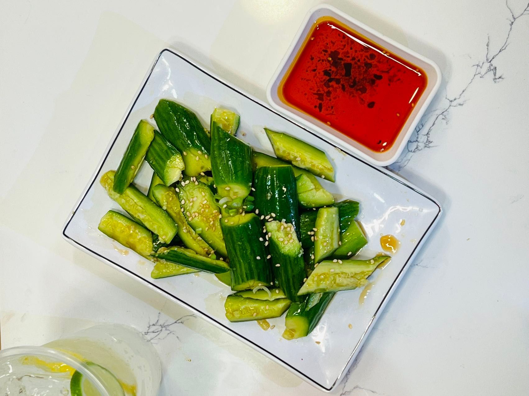 A white plate topped with cucumbers next to a bowl of dipping sauce.