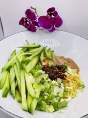 A white plate topped with noodles and vegetables next to a purple flower.