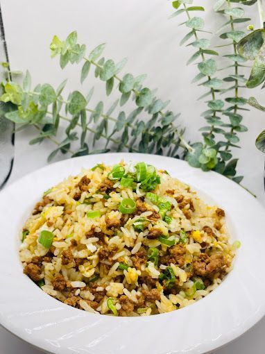 A bowl of rice with meat and green onions on a table.