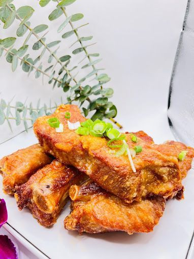 A white plate topped with fried pork ribs and green onions.