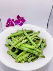 A white plate topped with green beans and a purple flower.