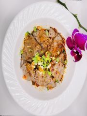 A white plate topped with meat and vegetables next to a purple flower.