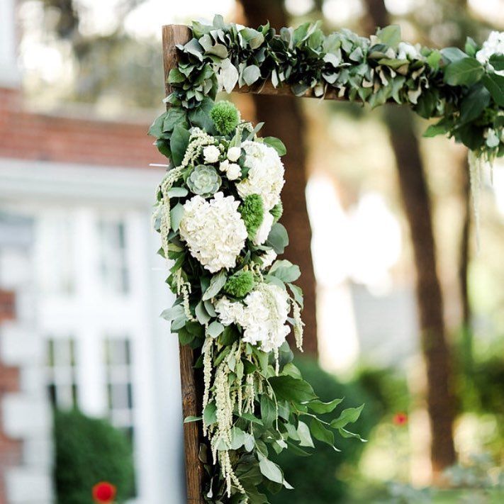 White floral arrangement and greenery on an outdoor wooden arch at a garden event
