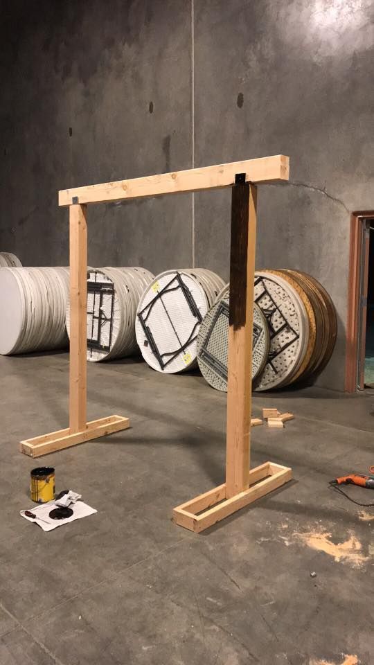 Wooden frame on a concrete floor with black vertical posts, in a workshop beside large rolls of material.