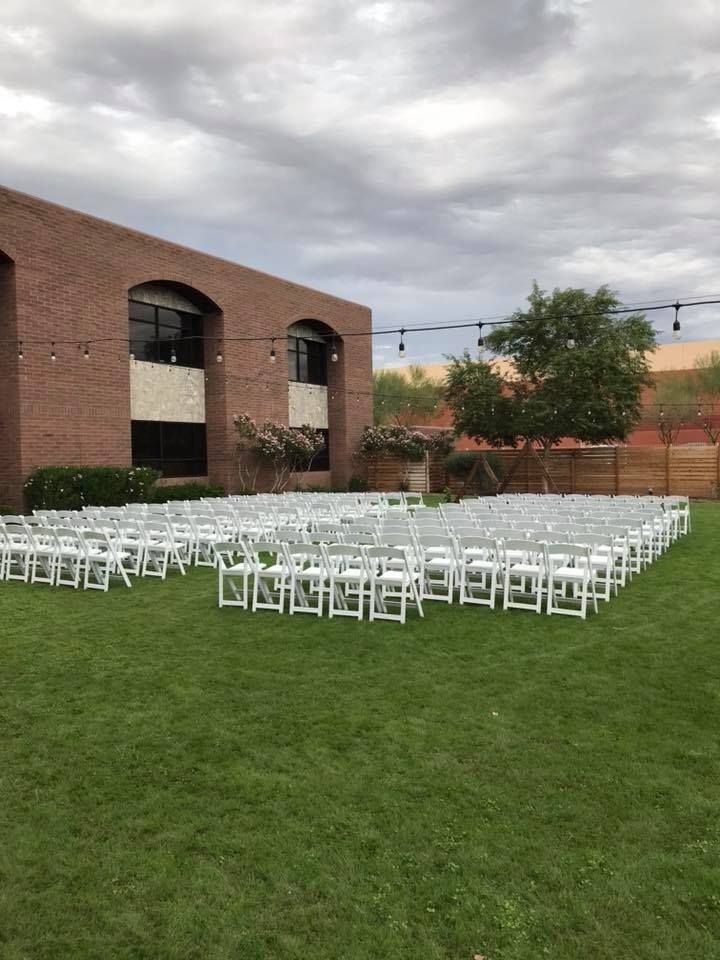White chairs arranged on a lawn beside a brick building under a cloudy sky