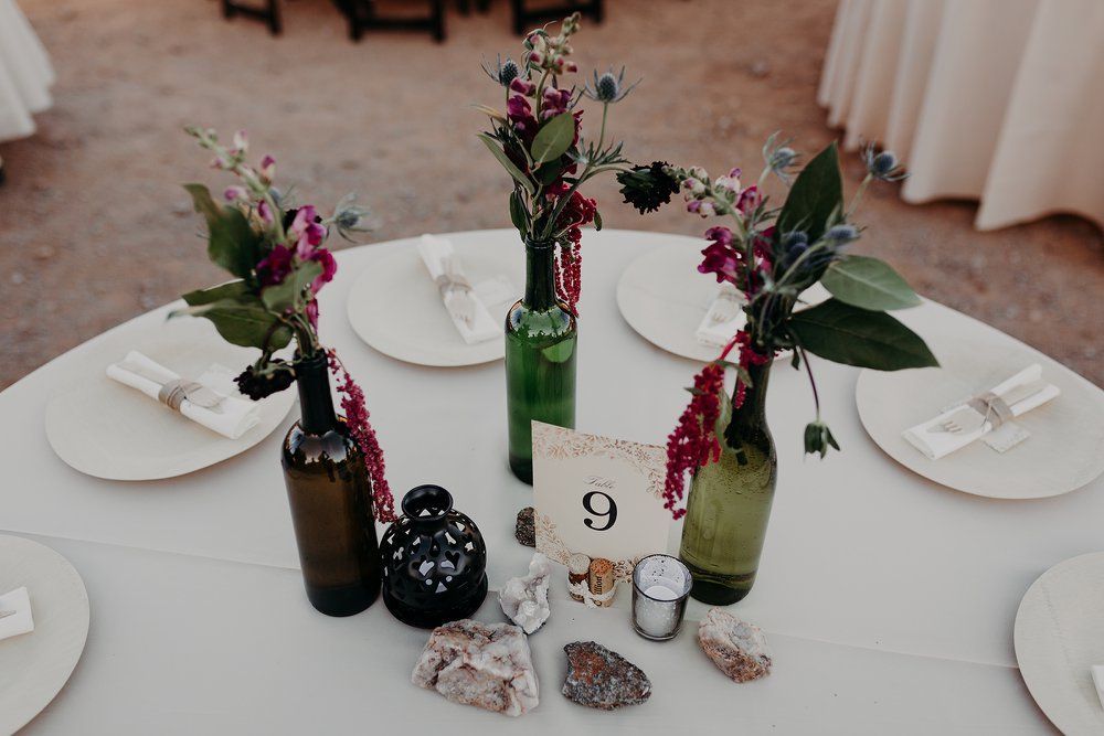 Round dining table with white plates, floral centerpieces, glass bottles, and table number 9