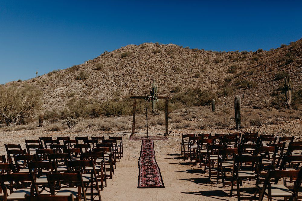 Outdoor wedding ceremony setup with rows of chairs facing a wooden arch in a desert landscape