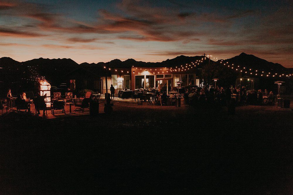 Nighttime outdoor festival with lit tents, string lights, and people gathered under a dark sky