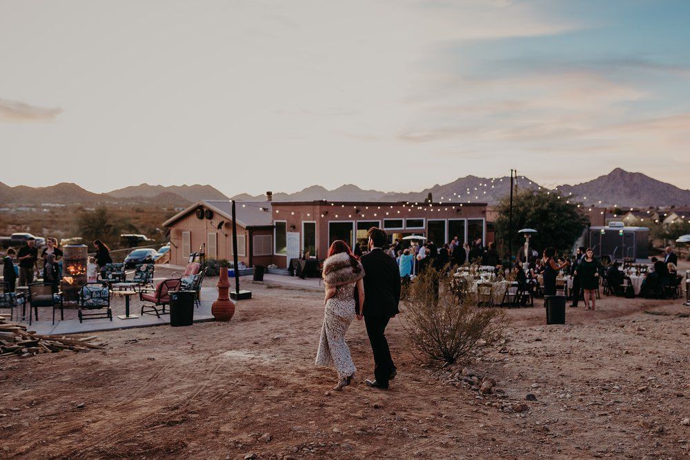 People standing in a rustic outdoor plaza at dusk, with a lit building and mountains in the background.