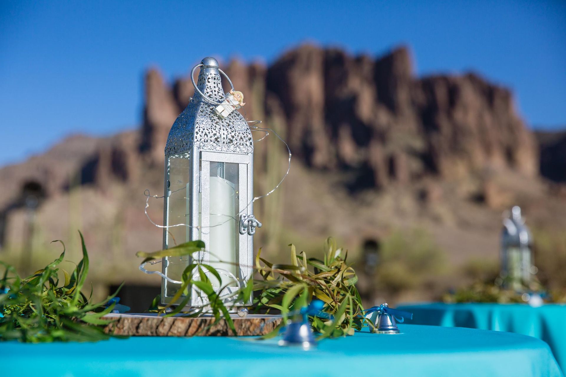 White lantern with greenery on a turquoise table, desert mountains blurred in the background.