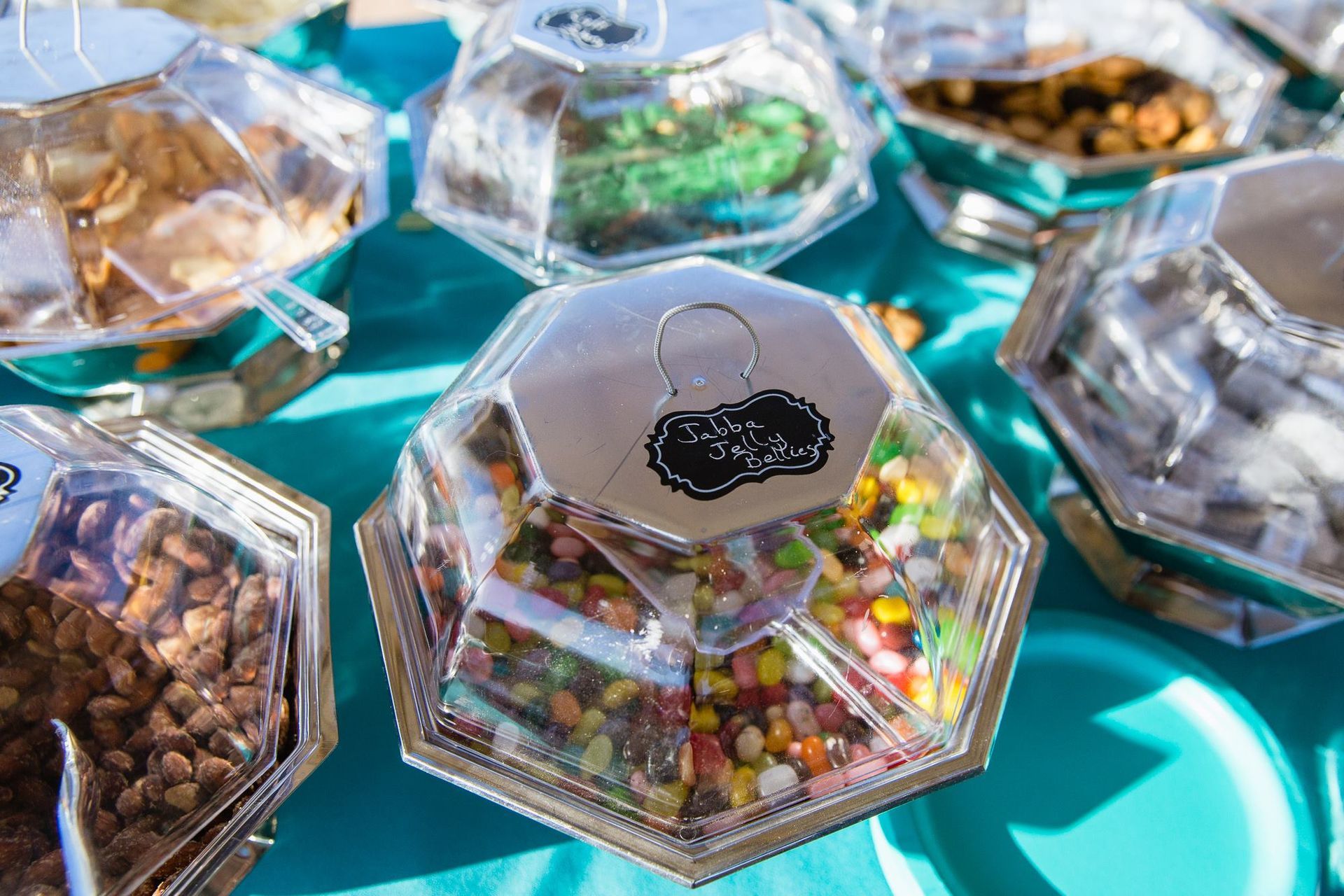 Clear plastic hexagon candy containers filled with assorted sweets on a turquoise tablecloth
