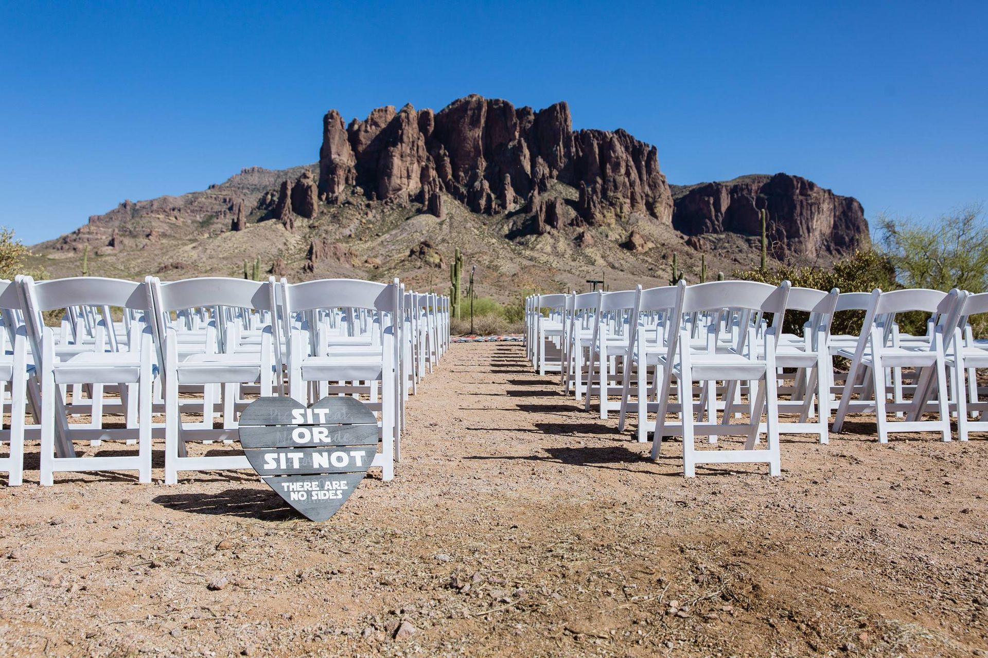 Rows of white folding chairs facing a desert mountain backdrop under a clear blue sky
