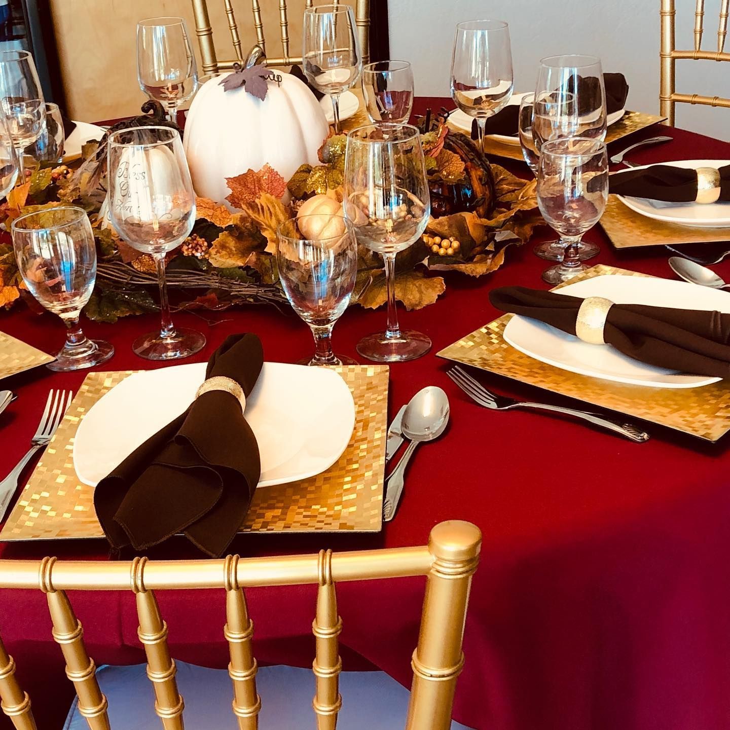 Elegant dining table set with red tablecloth, gold accents, white plates, and folded black napkins