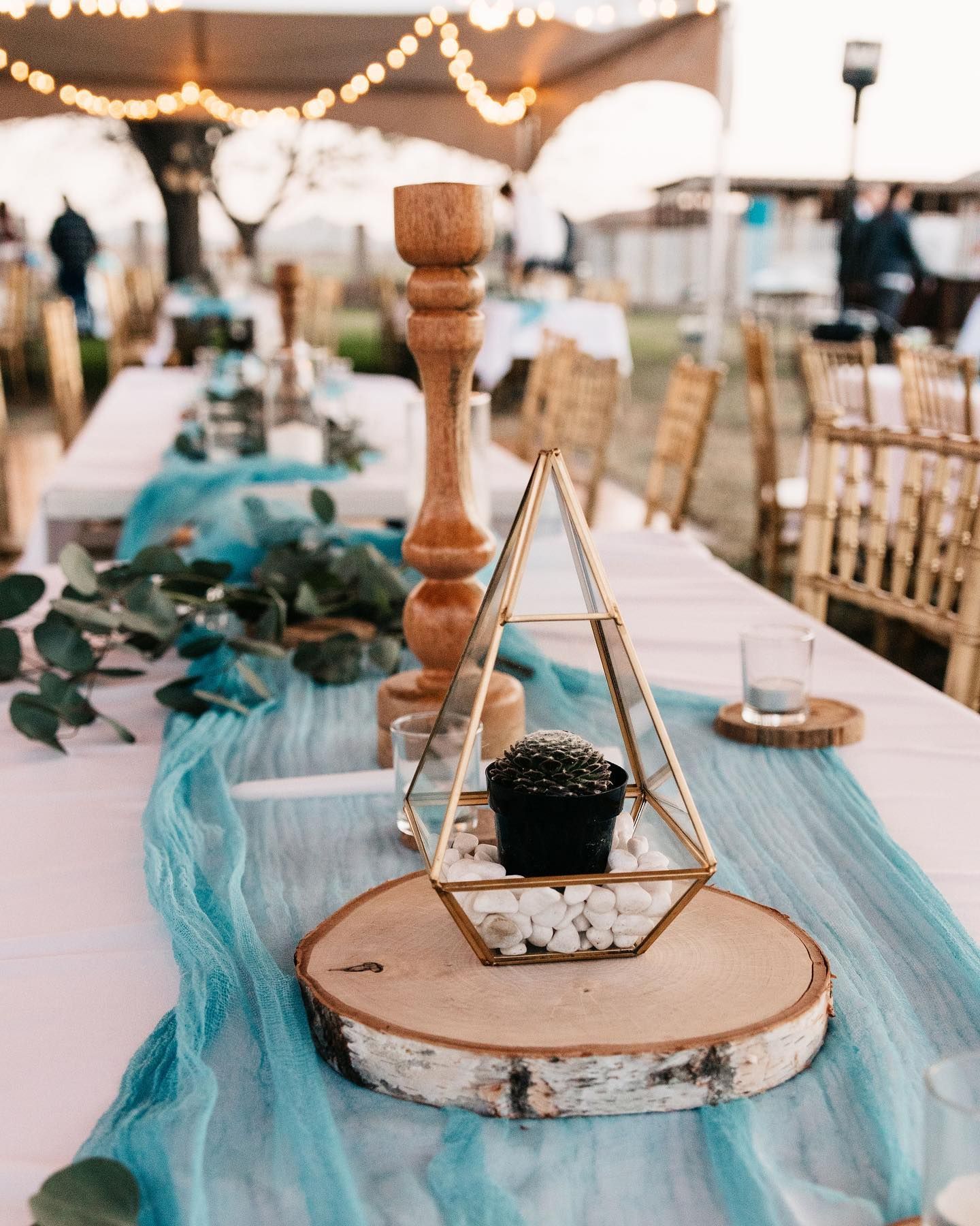 Rustic outdoor table centerpiece with wood slices, candles, teal fabric, and gold geometric decor