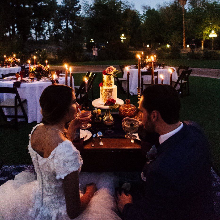 Couple seated at an outdoor candlelit dinner table with a tiered cake at dusk
