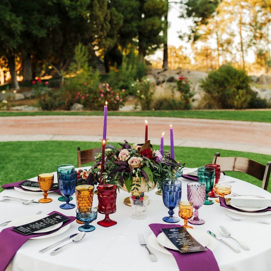 Outdoor table set with colorful glassware, candles, and flowers for a garden dinner