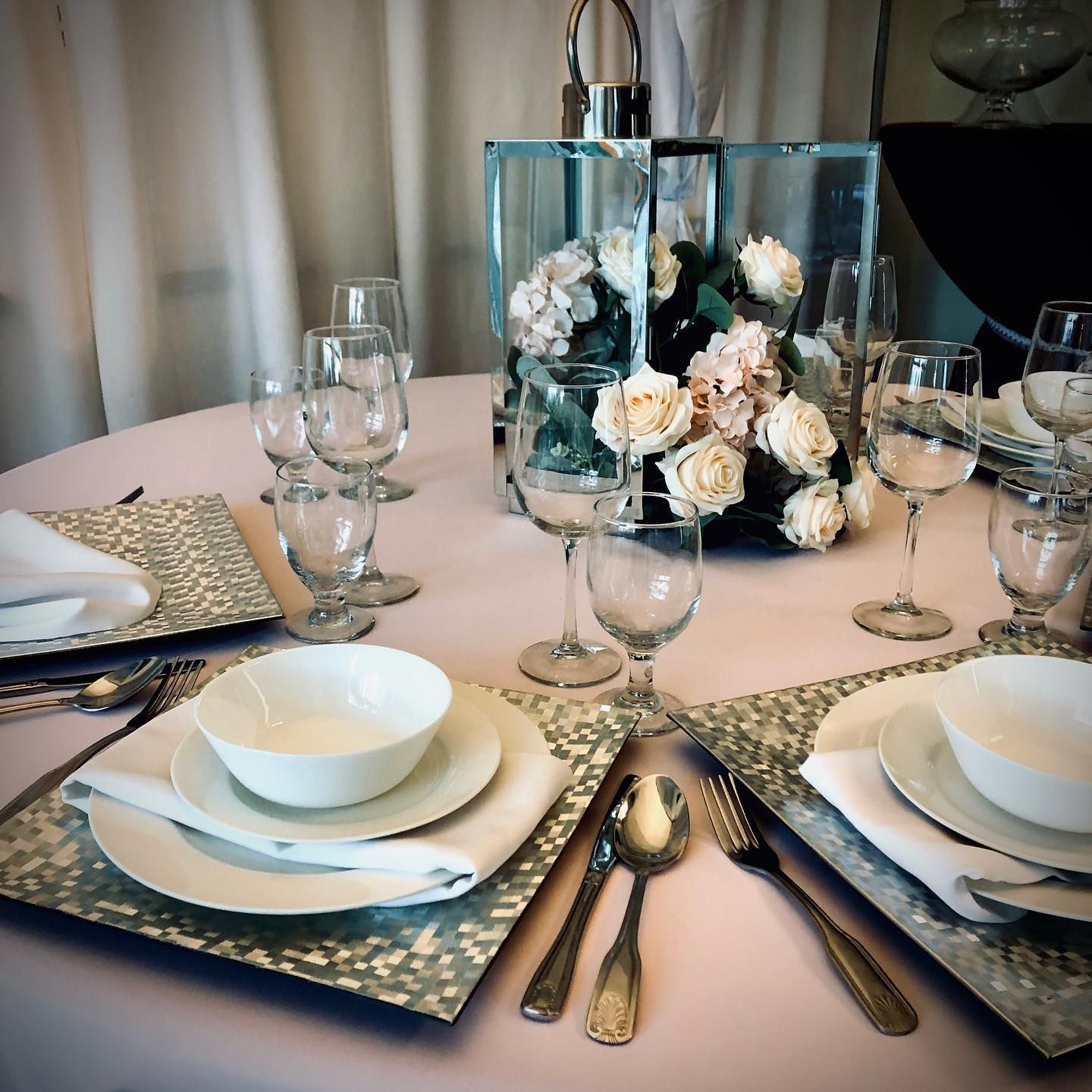Elegant dining table set with glassware, white dishes, and a floral centerpiece in a soft pink setting