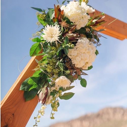 White floral arrangement draped over a wooden arch against a blue sky