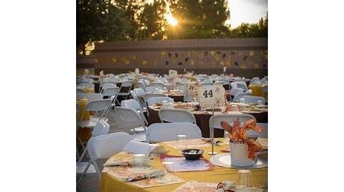 Outdoor banquet tables set with white chairs and yellow tablecloths at sunset