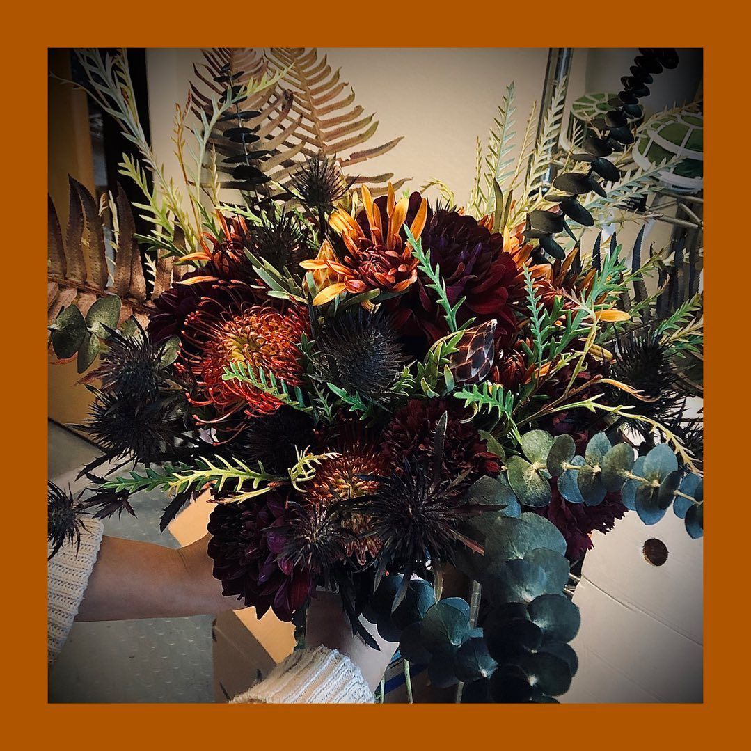 Autumn floral arrangement with dark red, orange, and green foliage in a vase