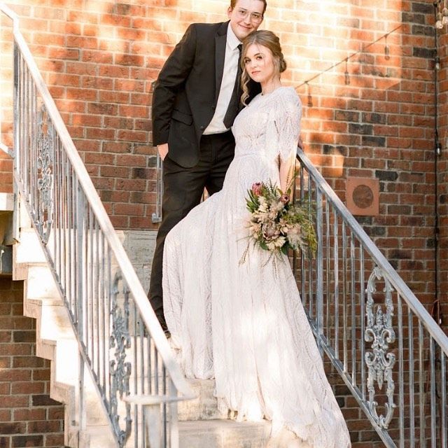 Couple posing on a brick stairway; woman in white dress holding bouquet, man in black suit behind her.