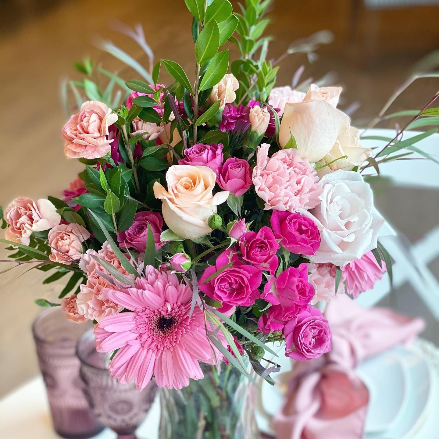 Pink and white flower bouquet in a glass vase on a table with candles