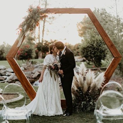 Bride and groom embracing in a garden ceremony framed by a wooden hexagon arch