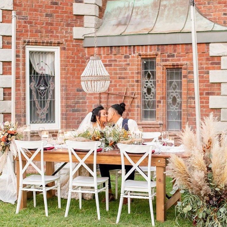 Outdoor wedding table with a couple kissing amid white chairs and floral decor in front of a brick building