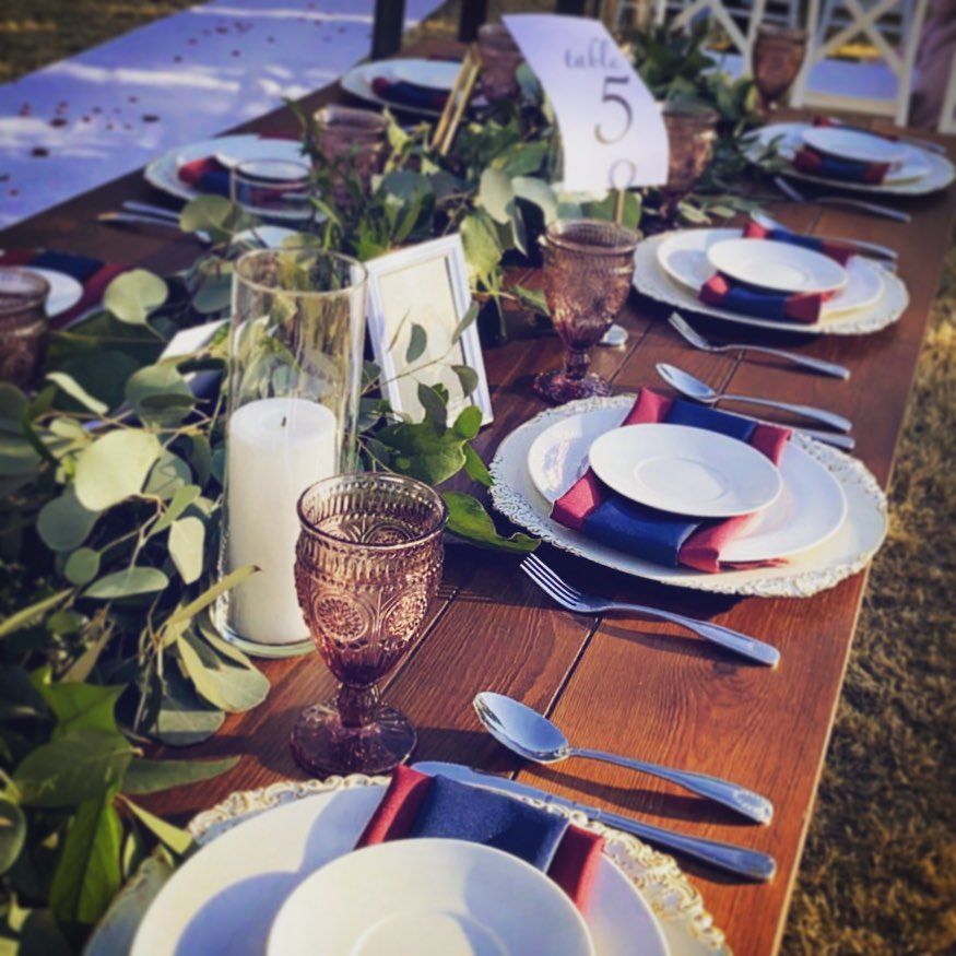 Outdoor dining table with white plates, red napkins, greenery, and a table number card reading 5