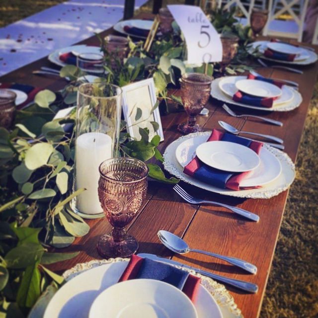 Decorated outdoor dining table with white plates, candles, greenery, and table number 5