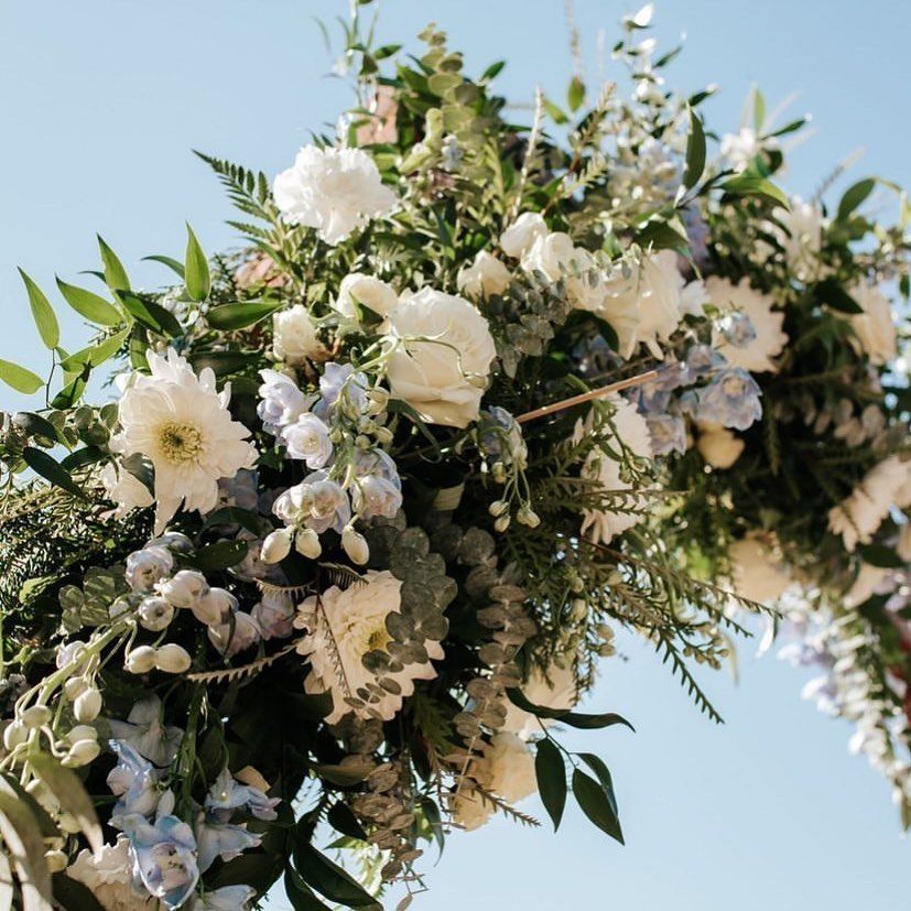 White floral arch with greenery against a blue sky