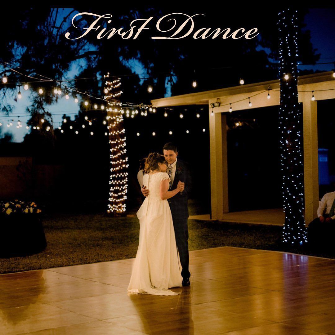 Bride and groom slow dance on a lit outdoor patio at night under “First Dance” sign.