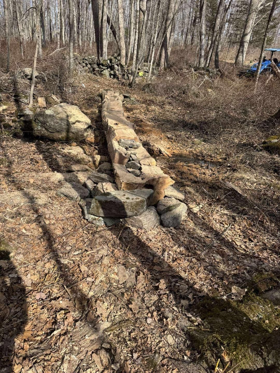 Stone and brick structure in a wooded area, possibly an old foundation or wall, surrounded by dry leaves and rocks.
