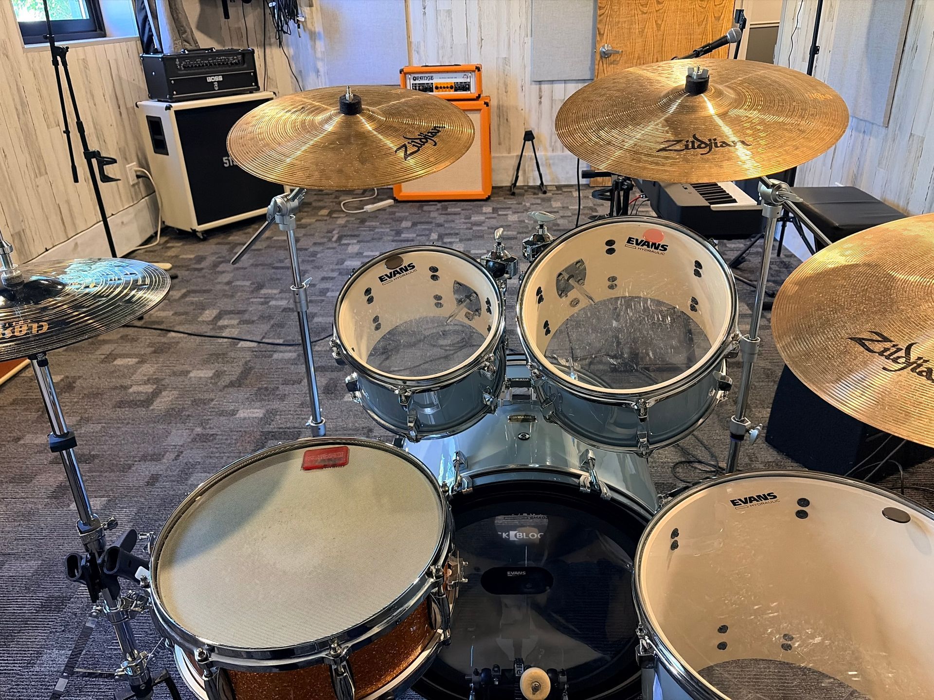 Drum kit with cymbals on a rug in a rehearsal room, with an orange amplifier in the background