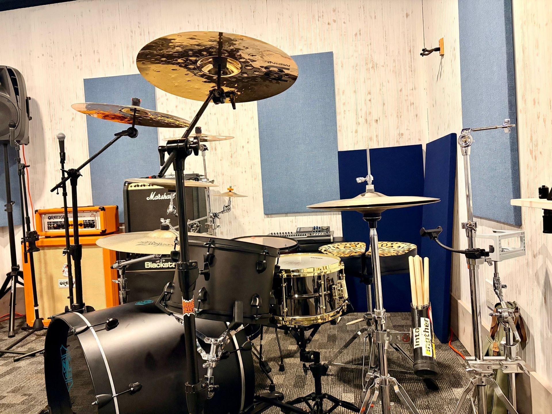 Drum kit in a small rehearsal room with cymbals, microphone stands, and scattered cables.