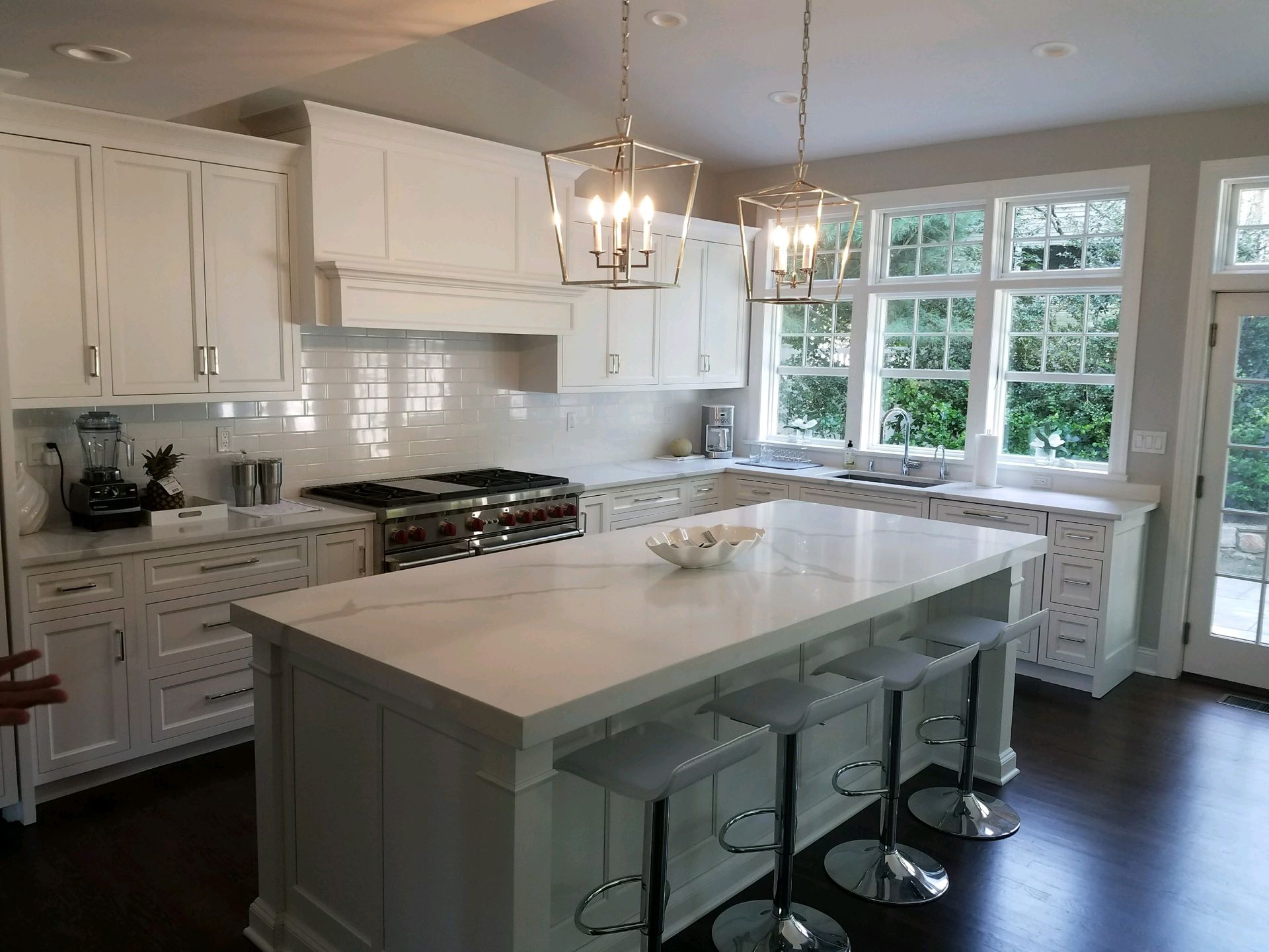 A kitchen with white cabinets , a large island , stools and a stove.