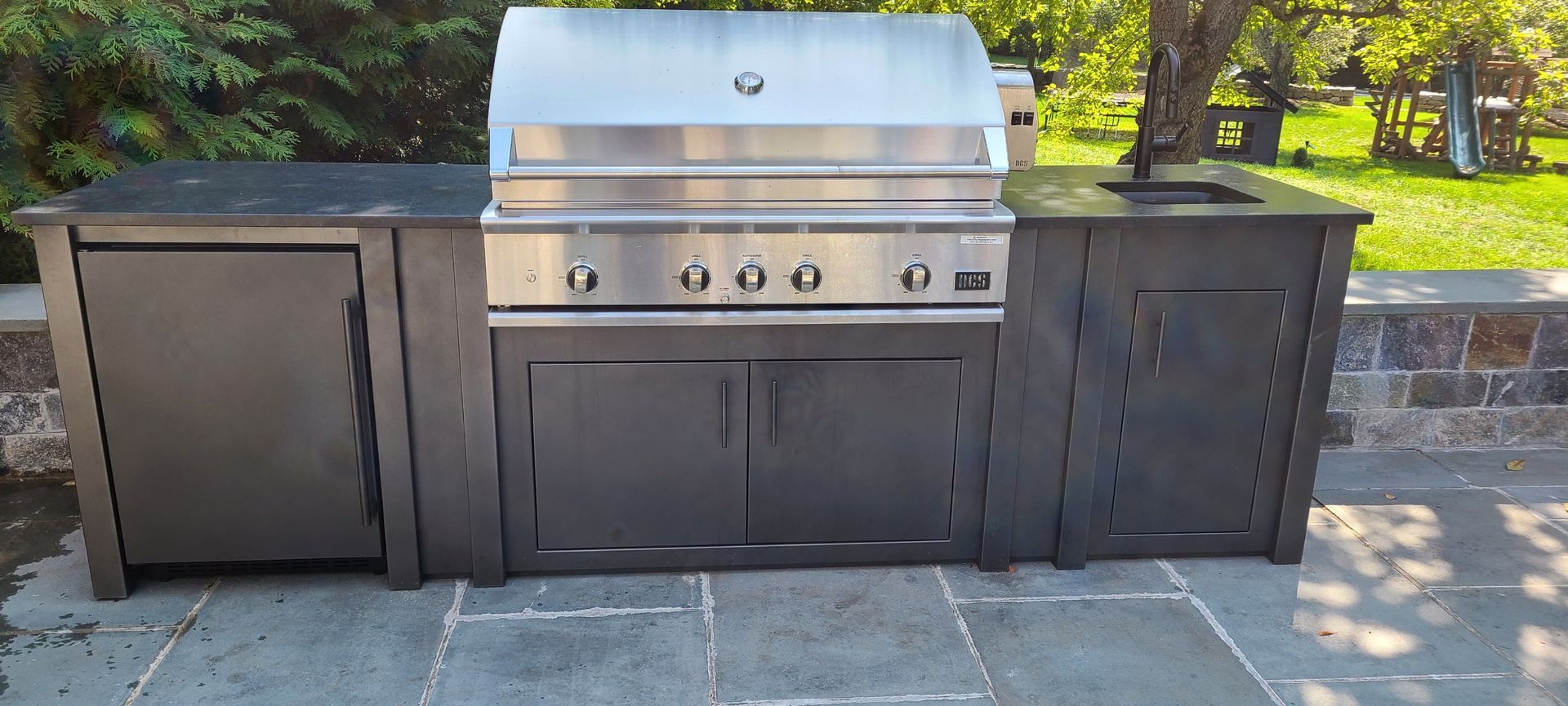 A stainless steel grill is sitting on top of a stone patio.