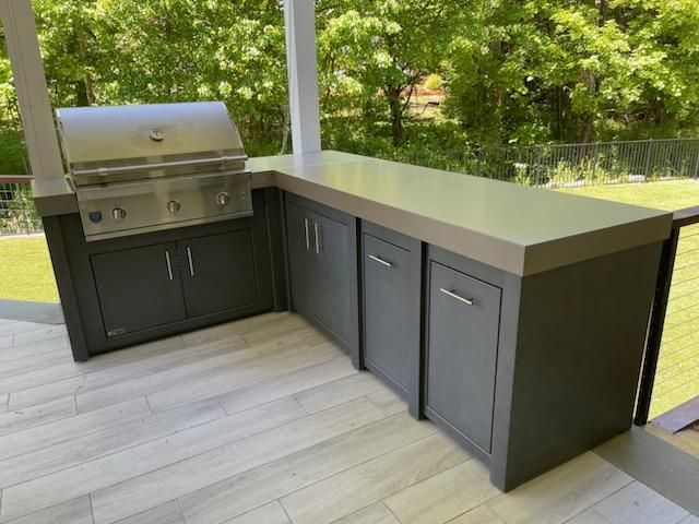 An outdoor kitchen with a grill and cabinets on a patio.