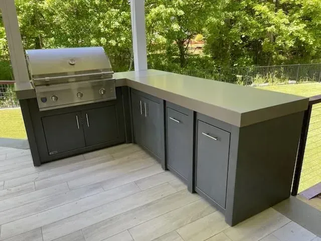 A large outdoor kitchen with a grill and cabinets on a patio.