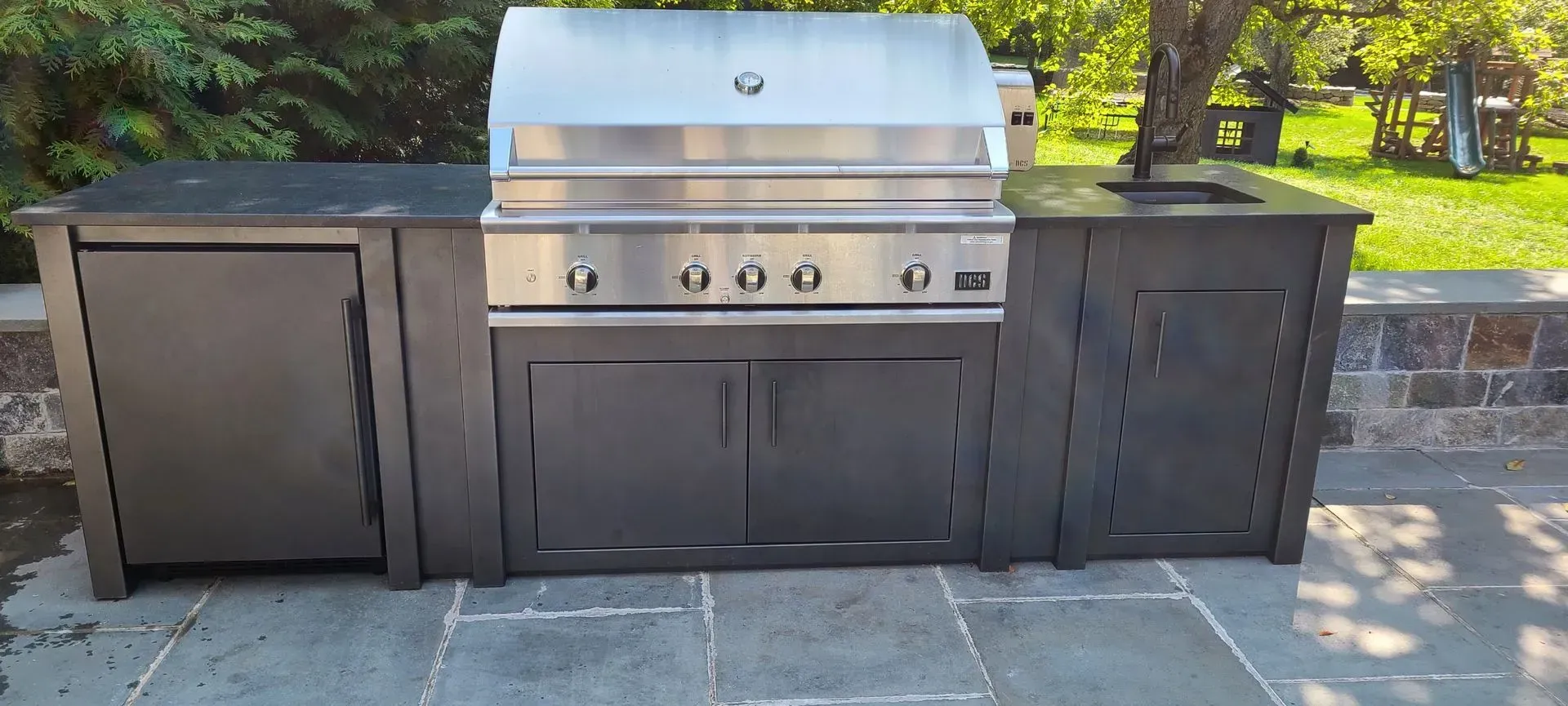 A stainless steel grill is sitting on top of a stone patio.