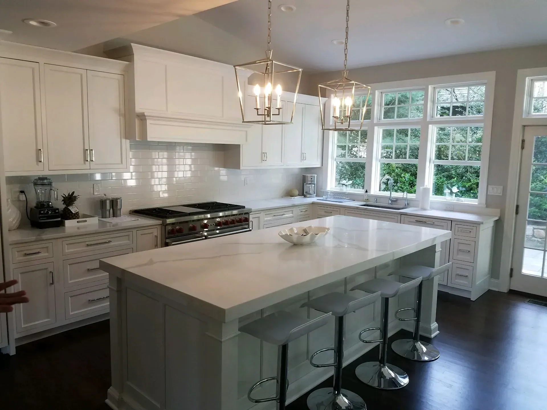 A kitchen with white cabinets, a large island, stools and a stove.