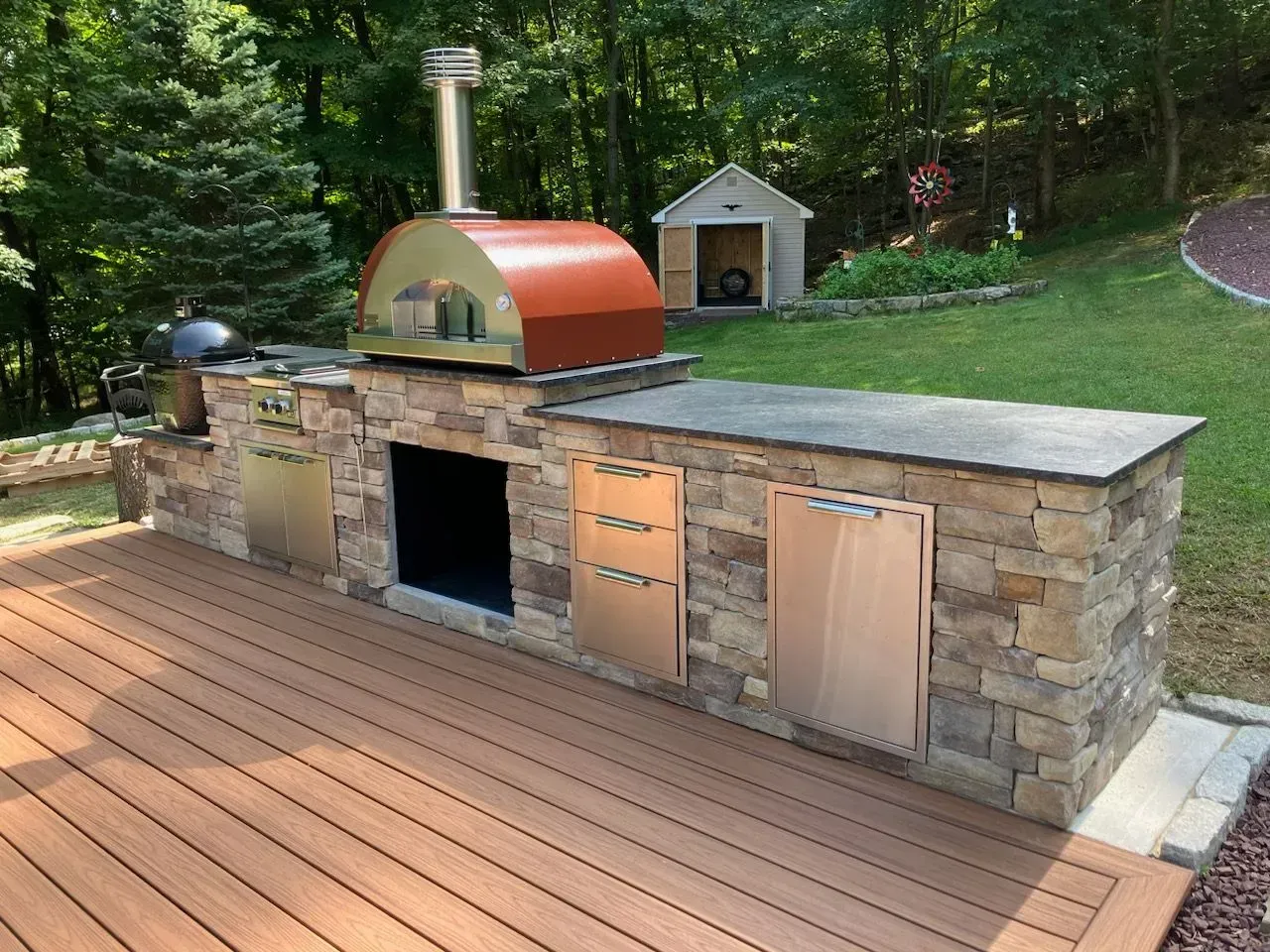 An outdoor kitchen with a pizza oven and a grill on a wooden deck.
