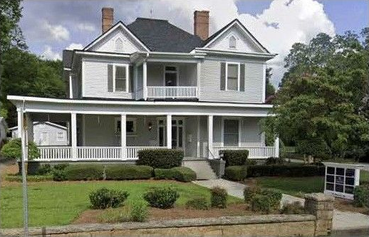 White two-story house with a front porch, manicured lawn, and trees
