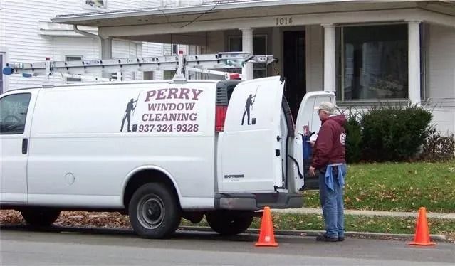 A white Perry Window Cleaning van is parked on a street with traffic cones; a person stands at the open back doors.