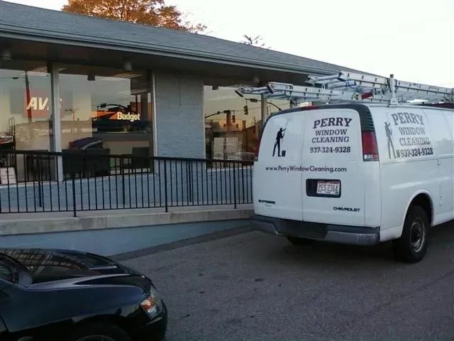 A white Perry Window Cleaning van parked in front of a commercial building with large glass windows and a black railing.
