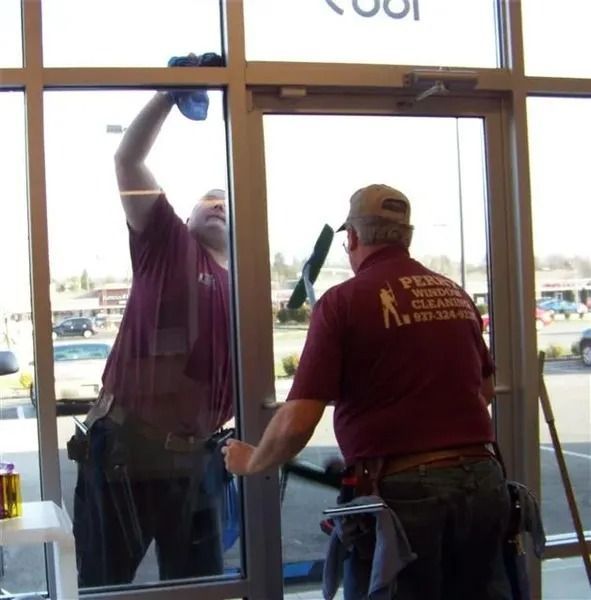 Two window cleaners in maroon shirts clean the glass of a store entrance.