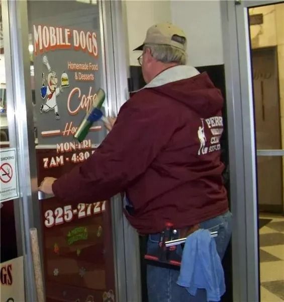 A person in a maroon jacket cleans a glass door displaying a 