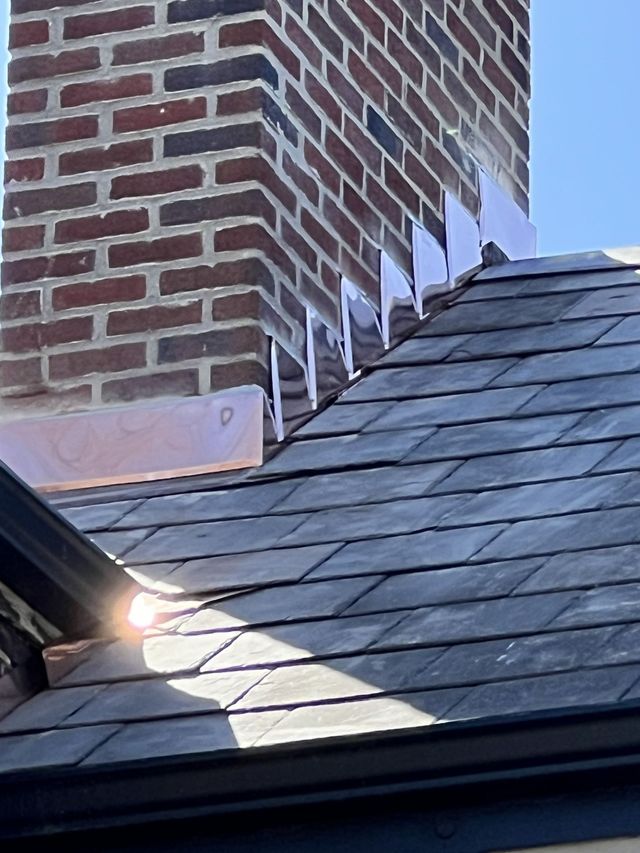 Brick chimney and dark shingled roof with sunlight on the eaves against a blue sky
