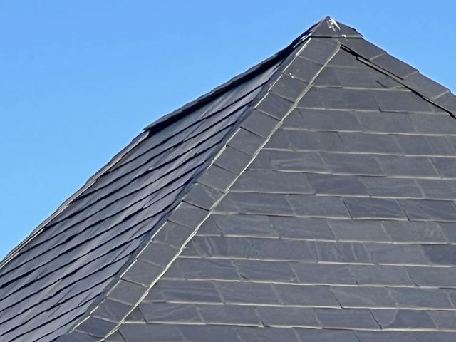 Dark gray shingled roof with a peaked ridge against a blue sky