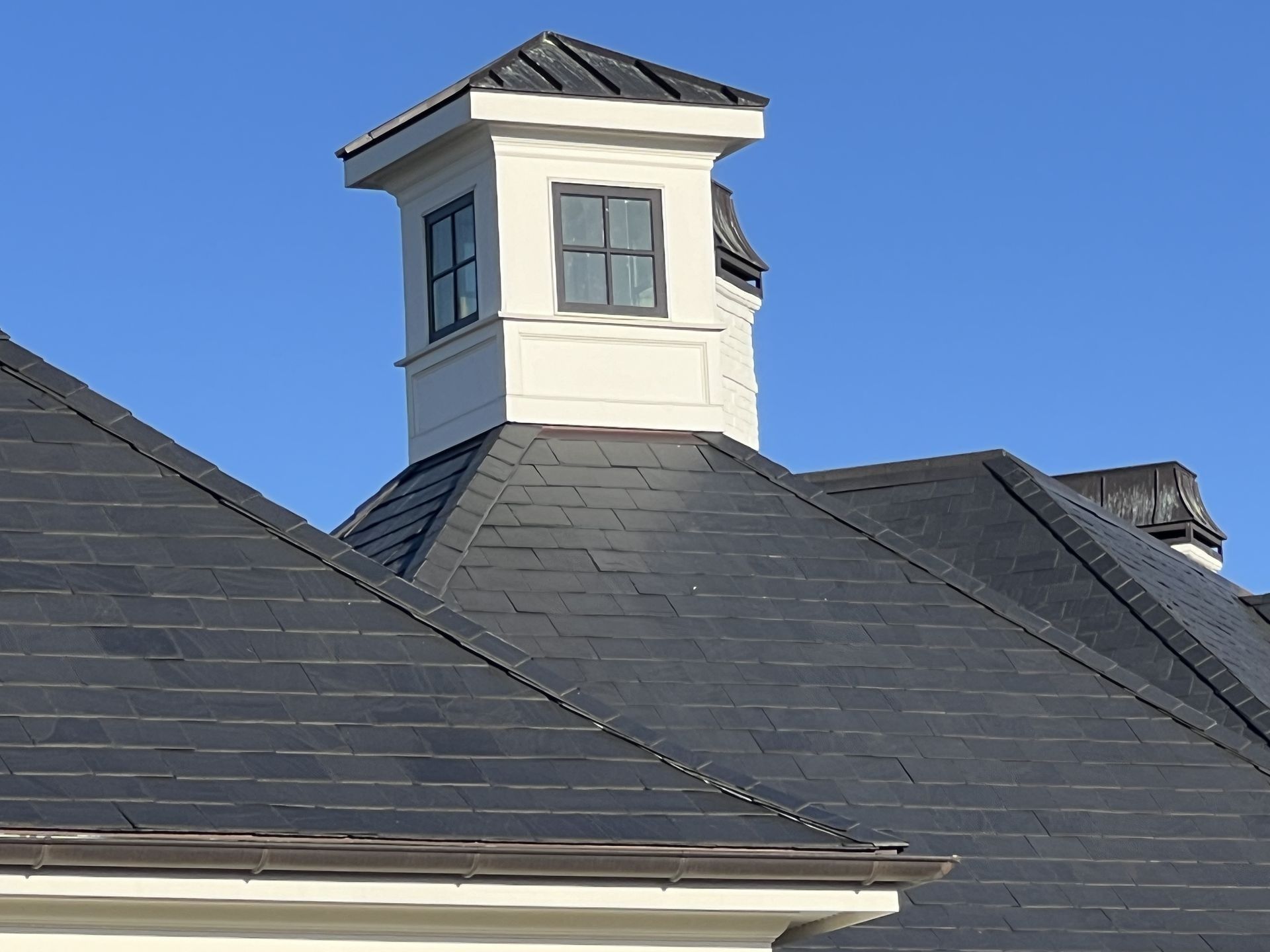 Dark shingled roof with a white rooftop cupola against a blue sky